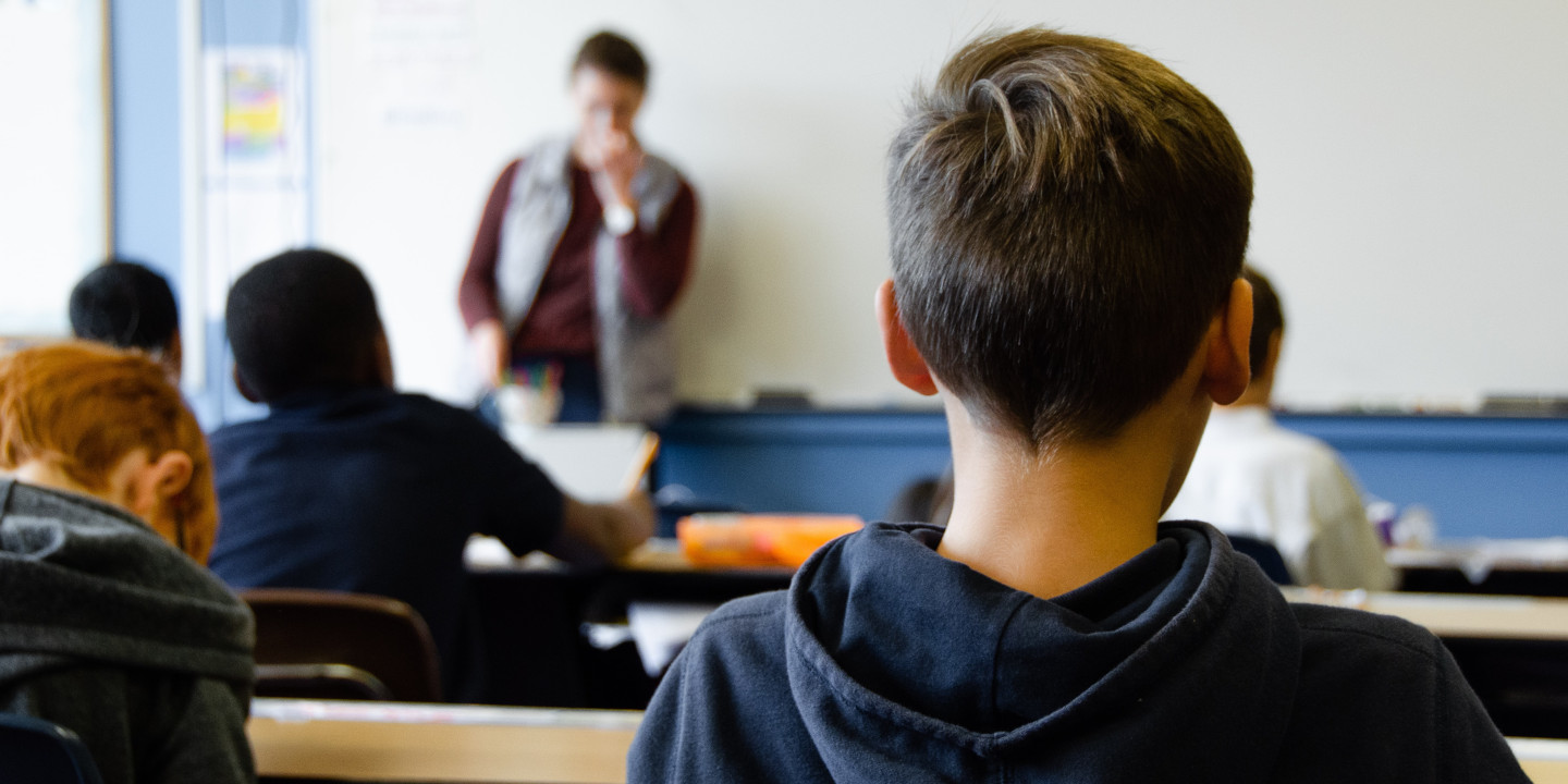 Jugendliche, die in einr Schulklasse sitzen und vorne steht eine Lehrperson