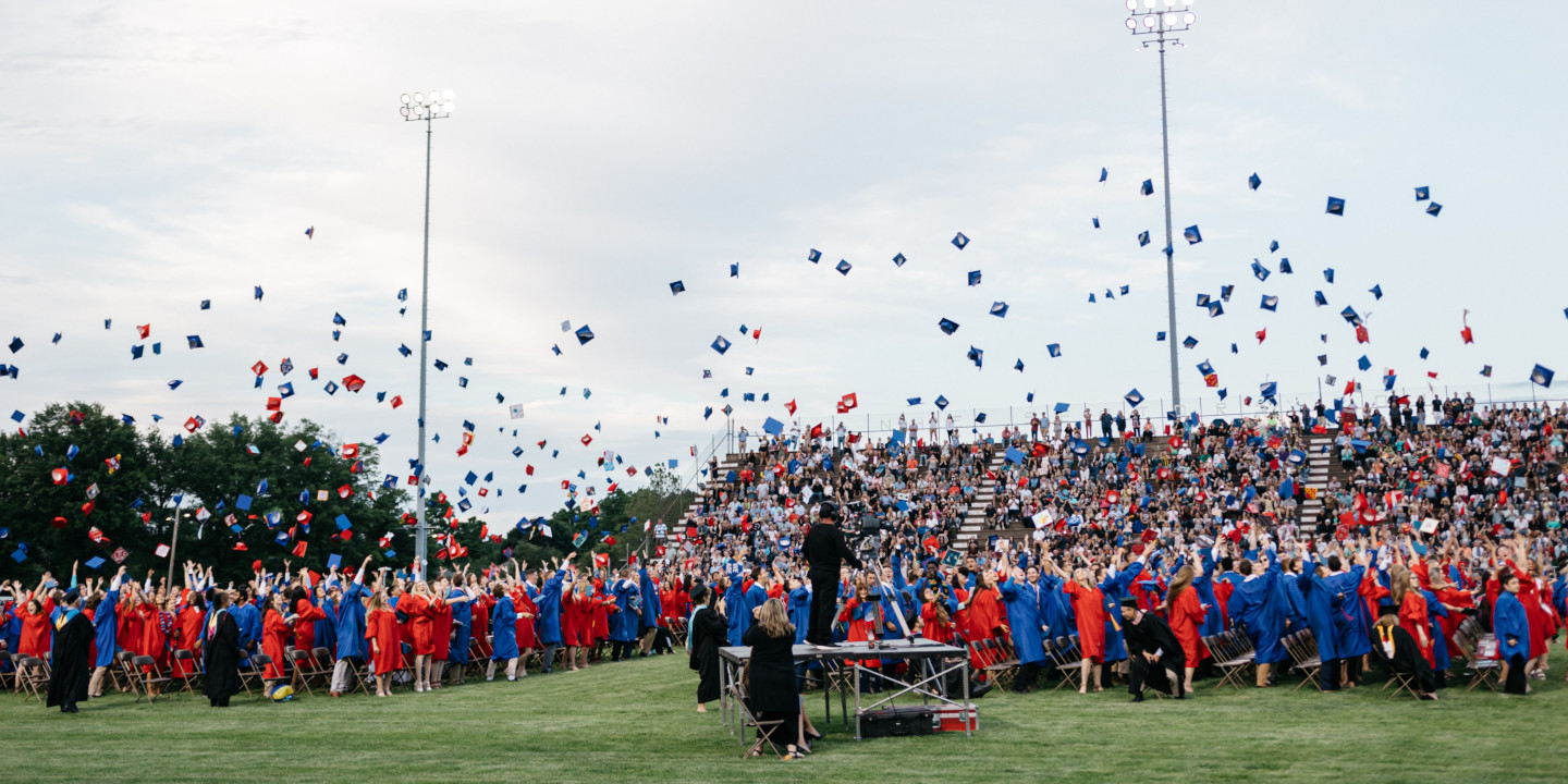 High School Abschluss und alle werfen ihre roten oder blaueb Hüte in die Luft