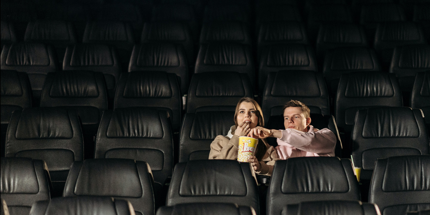 Eine junge Frau und ein junger Mann sitzen in einem leeren Kino und essen Popcorn.